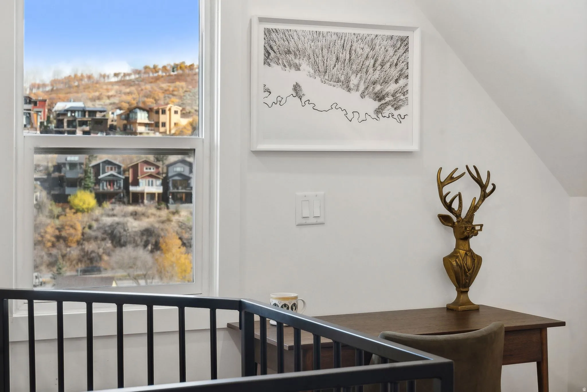 White framed window overlooking a hillside with residential structures and natural foliage