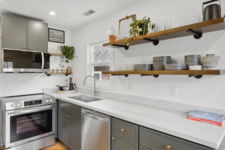 Kitchen featuring stainless steel appliances, open wood-finish shelving, gray cabinetry, and light countertops