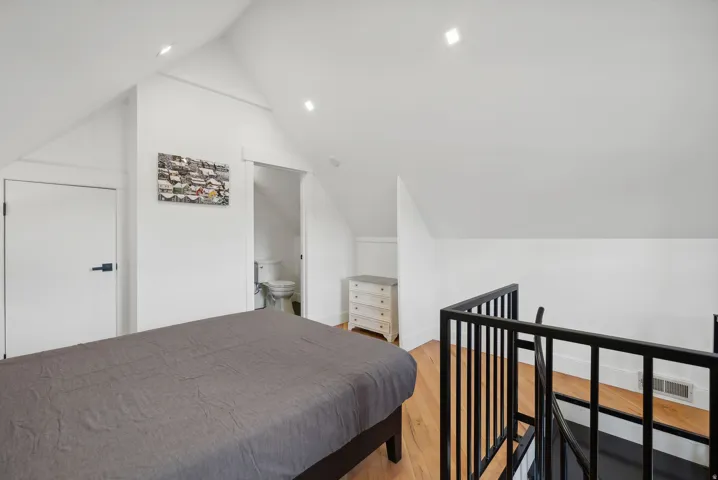Attic bedroom featuring vaulted ceilings, light wood-finish flooring, recessed lighting, and a black metal railing