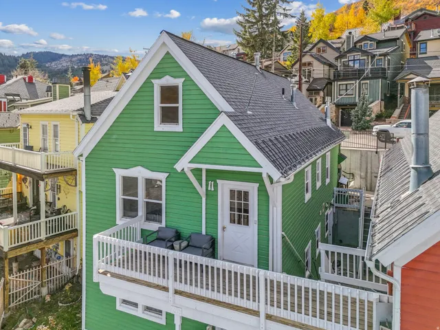 Green clapboard siding with white trim, featuring a dark shingle roof and a front balcony with white railings