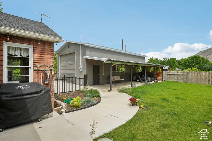 Expansive backyard featuring a manicured lawn, concrete pathway, and a detached structure with a covered patio area