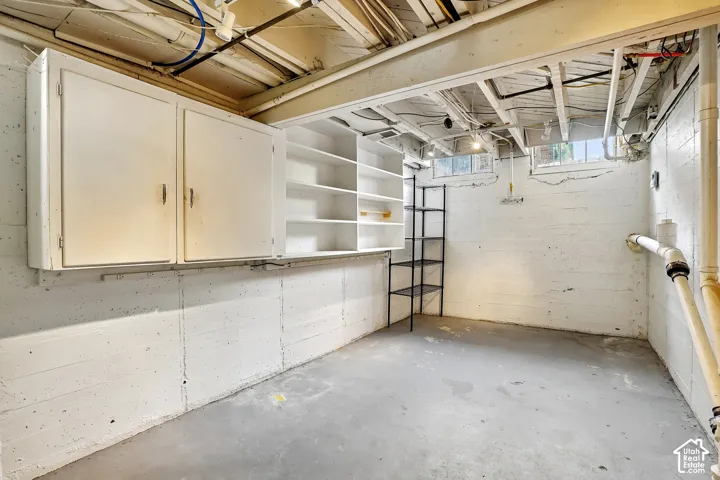 Spacious lower level featuring white-painted concrete walls, exposed ceiling joists, and a concrete floor