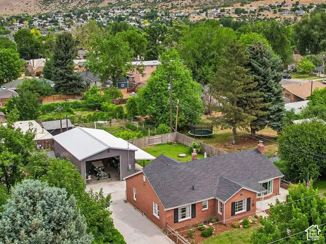 Brick exterior residence with dark shingle roofing, featuring a paved driveway and mature landscaping