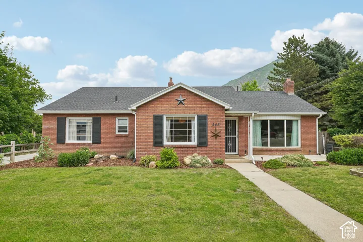 Classic brick exterior with a gray shingle roof, featuring a bay window, window shutters, and a concrete pathway leading to the entry