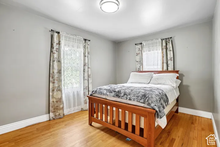 Light-filled room featuring wood-finish flooring, two windows with window treatments, a flush mount ceiling light fixture, and light gray wall paint