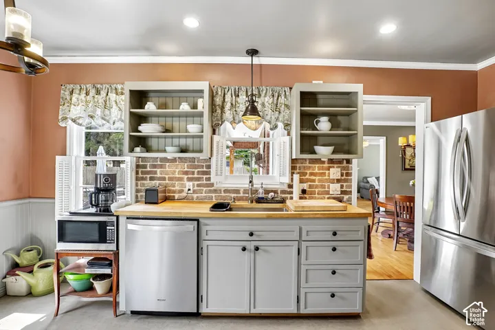 Kitchen featuring stainless steel appliances, light gray cabinetry with black hardware, wood-finish countertops, and a brick-finish backsplash