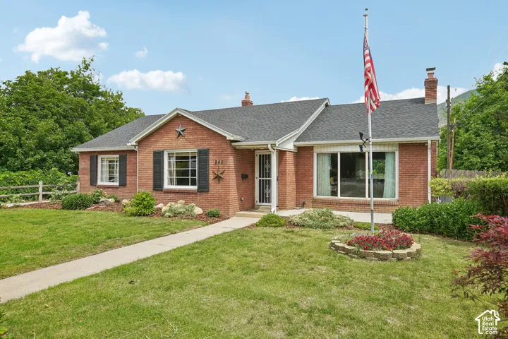 Brick facade residence featuring a dark shingle roof, decorative shutters, and established landscaping