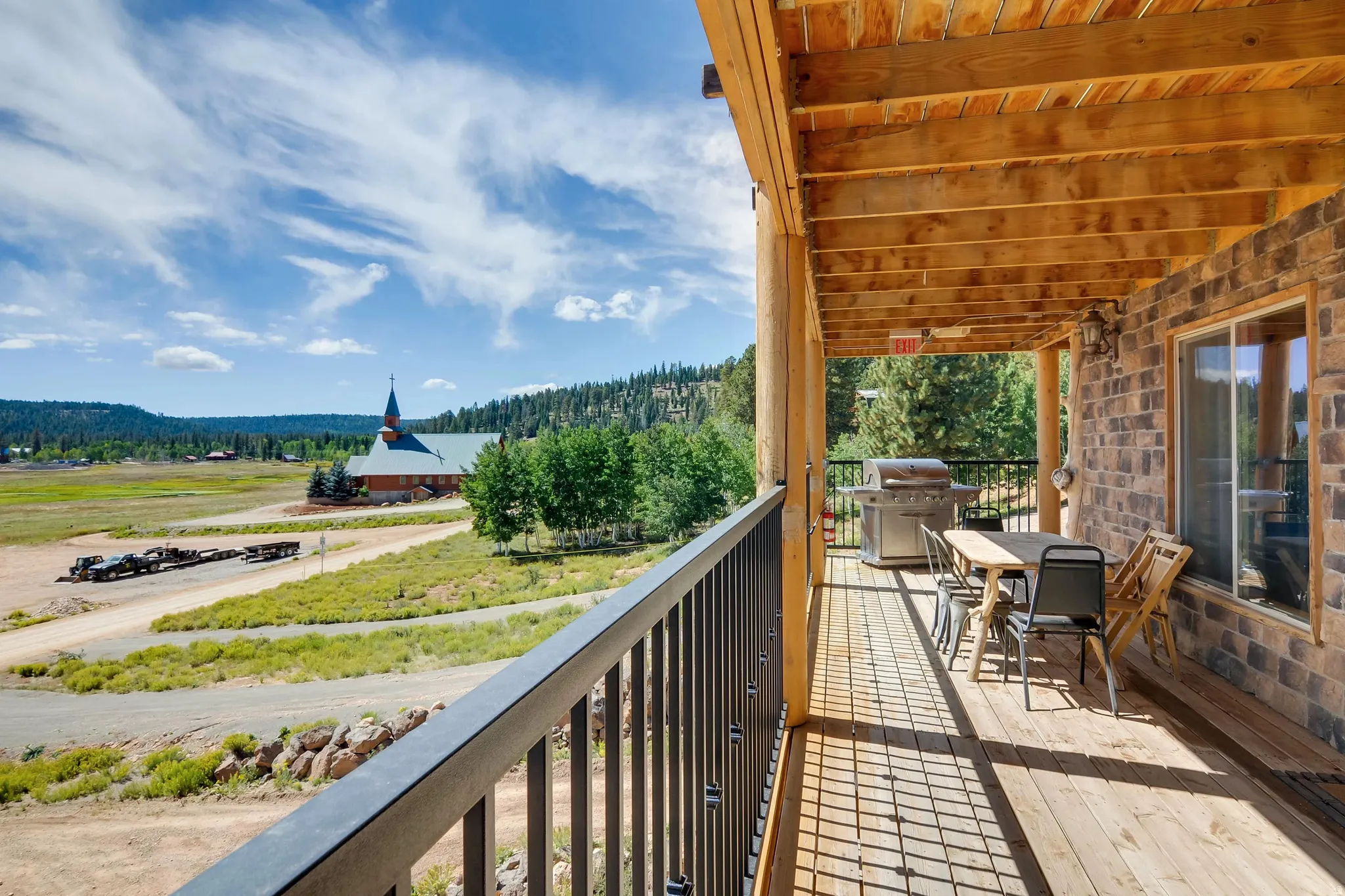 Expansive wooden deck with a durable black metal railing, featuring a log beam ceiling and a brick exterior wall