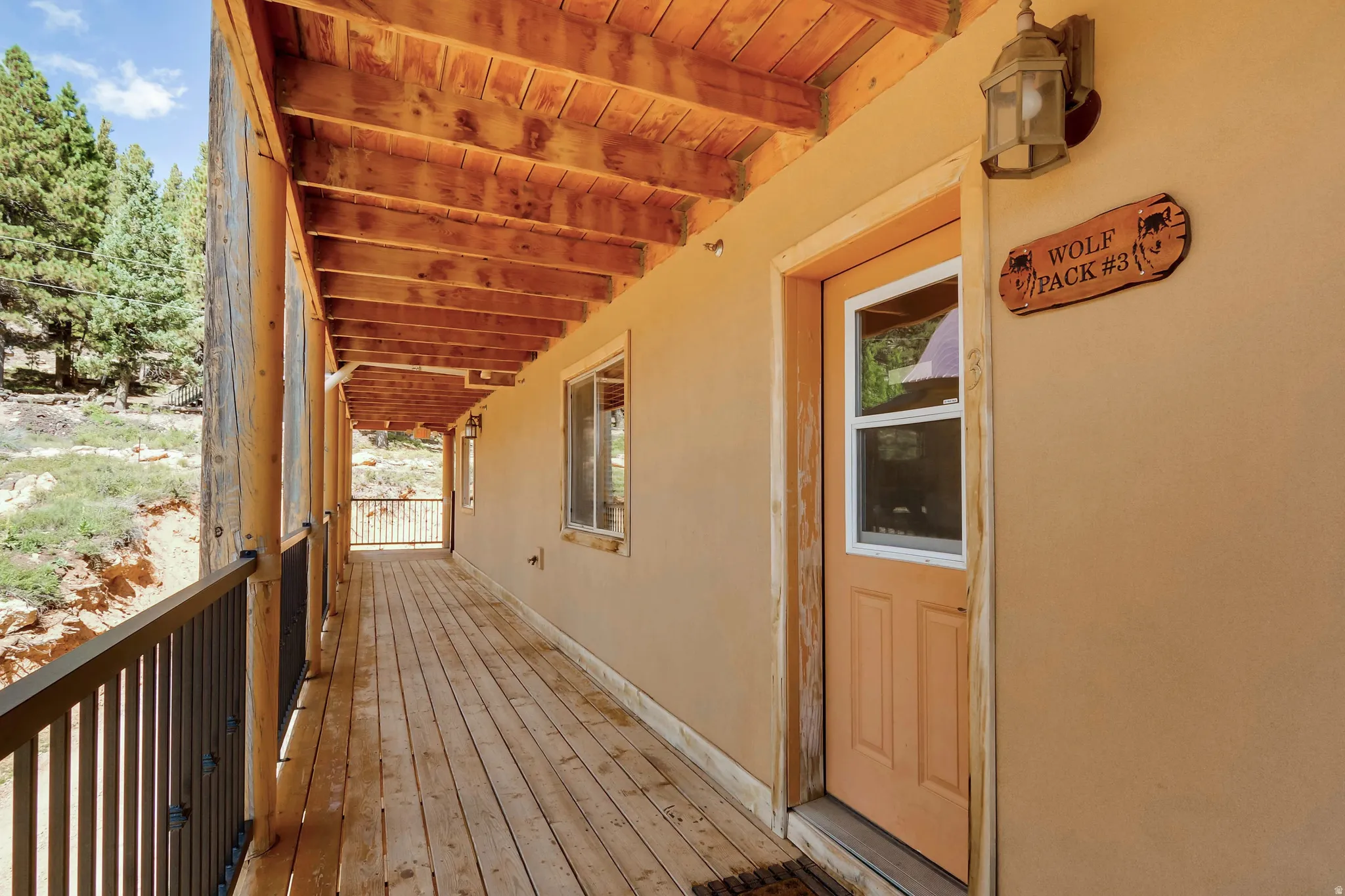 Expansive covered porch featuring wood-finish flooring, exposed wood beam ceiling, natural wood posts, and a durable metal railing