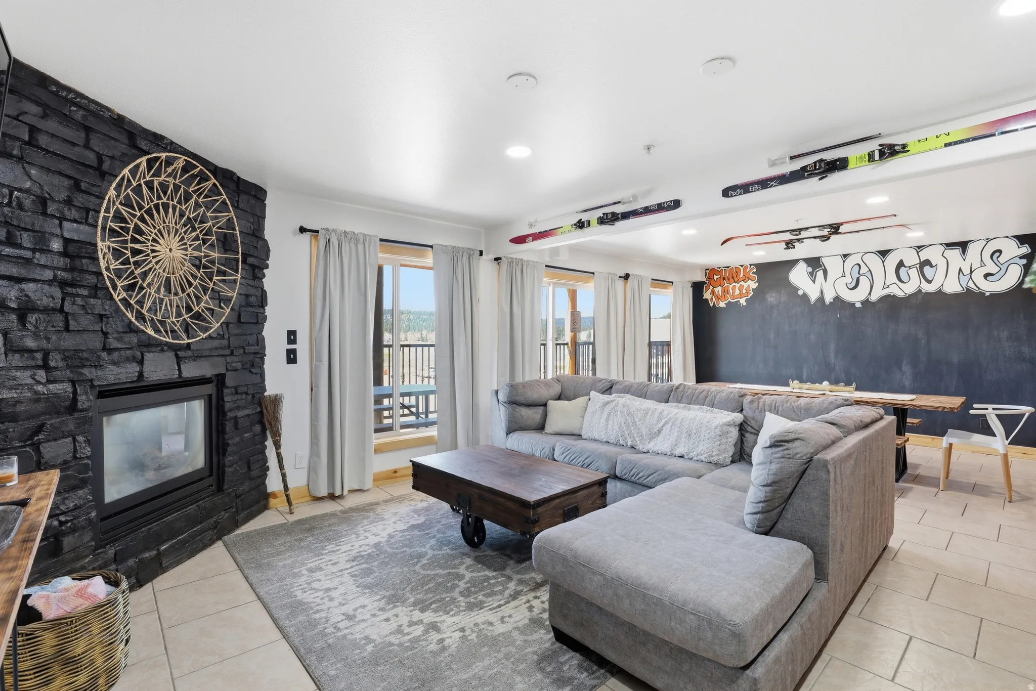 Spacious interior featuring a black stacked stone fireplace, tile flooring, and multiple windows with outdoor access