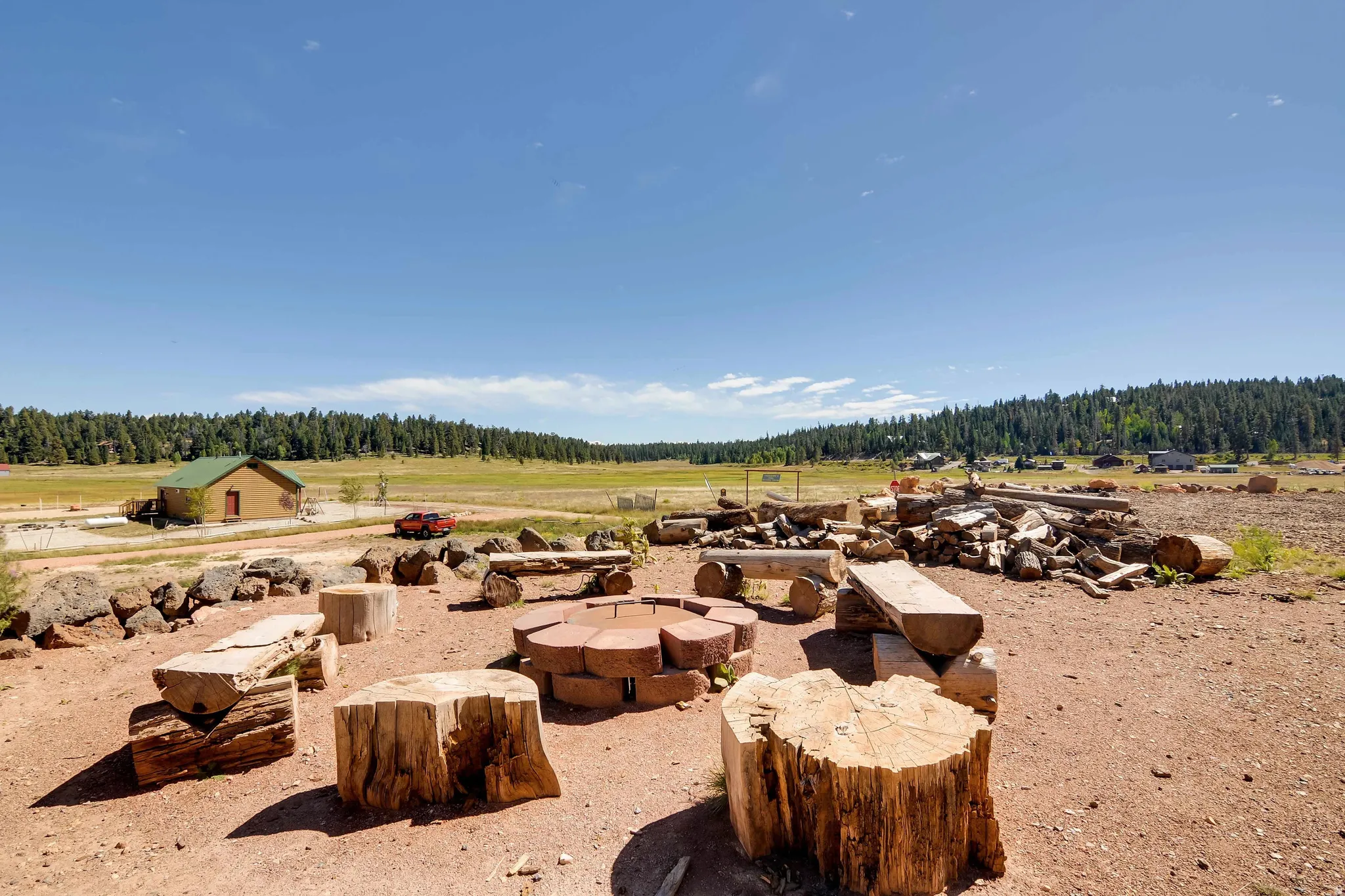 Outdoor fire pit area with log seating, surrounded by natural terrain and distant treelines
