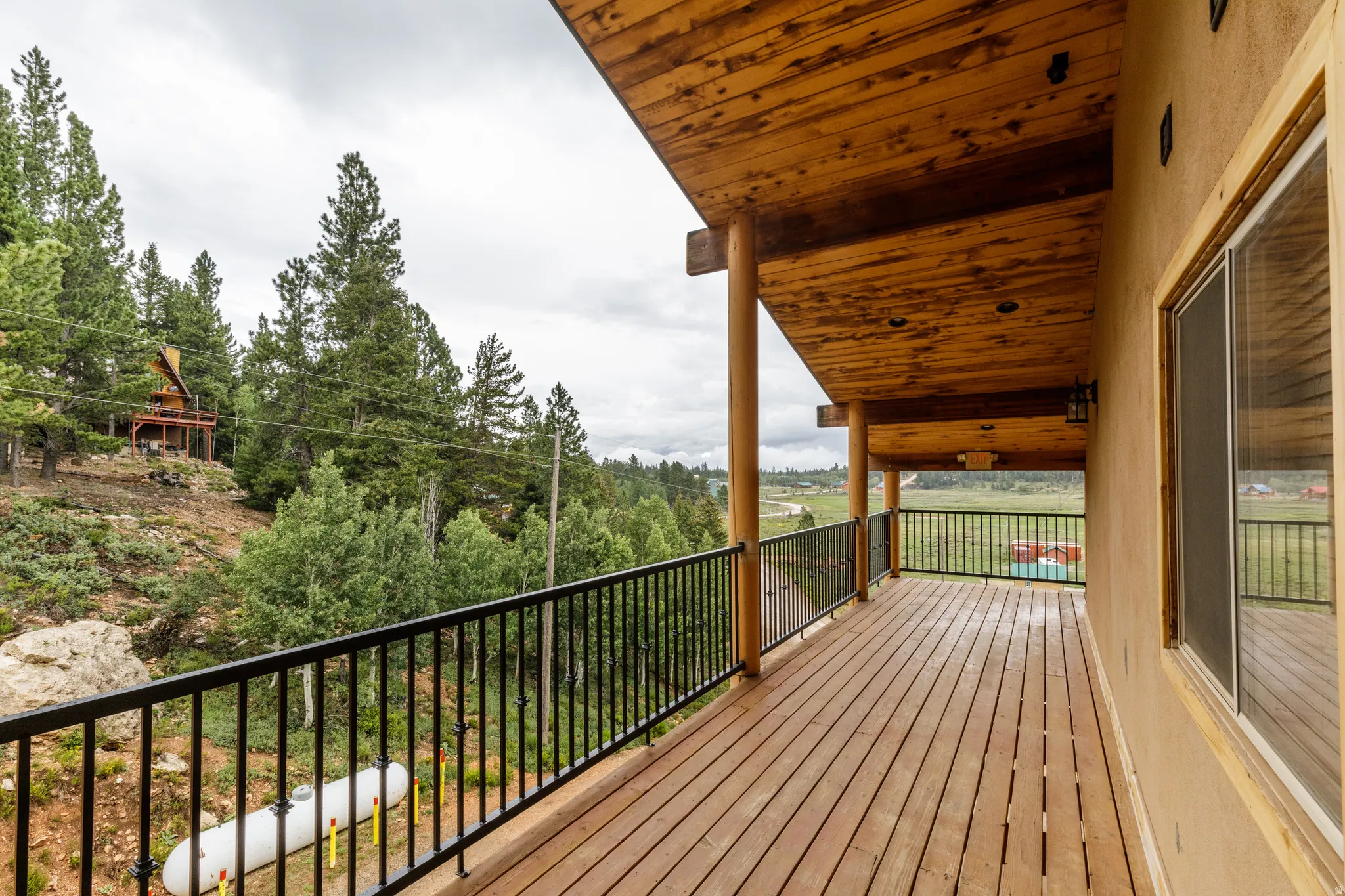 Expansive wood deck with black metal railings, a natural wood ceiling, and round support columns