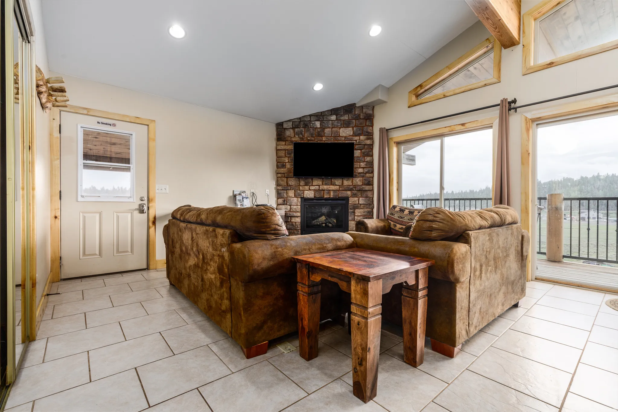 Stone-faced fireplace with hearth, ceramic tile flooring, and vaulted ceiling with exposed wood beams