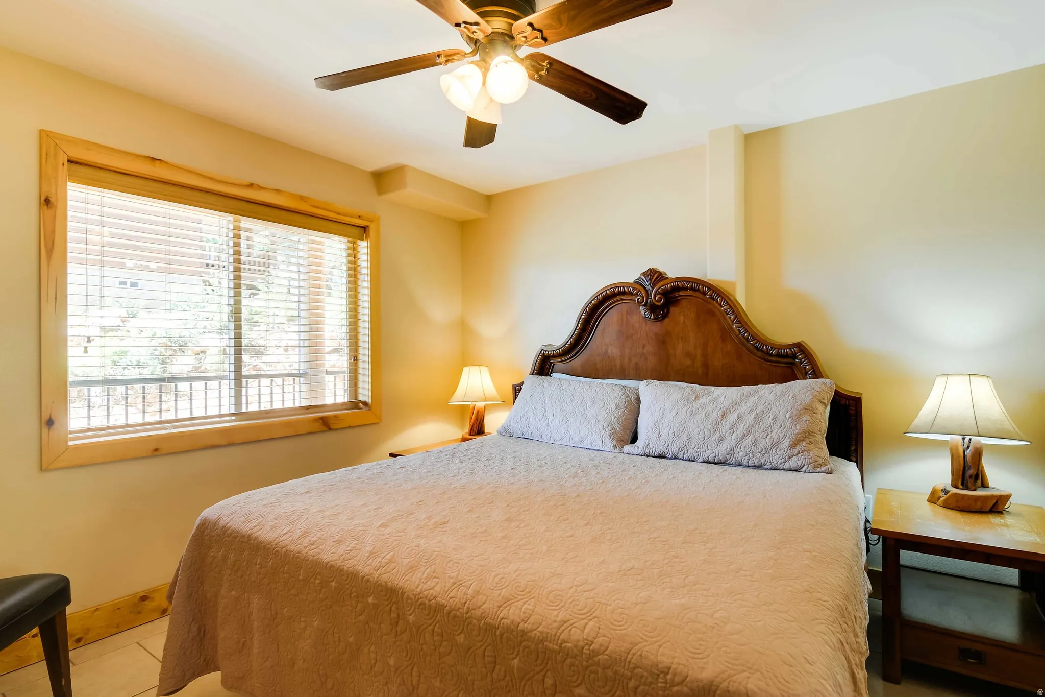 Bedroom featuring a wood-finish ceiling fan with integrated lighting, wood-trimmed window with horizontal blinds, and tile flooring