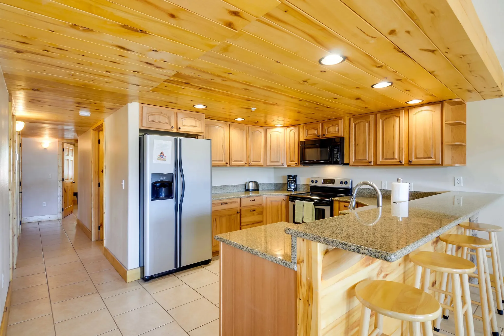 Kitchen featuring wood-finish cabinetry, granite-style countertops, stainless steel refrigerator, and recessed ceiling lighting
