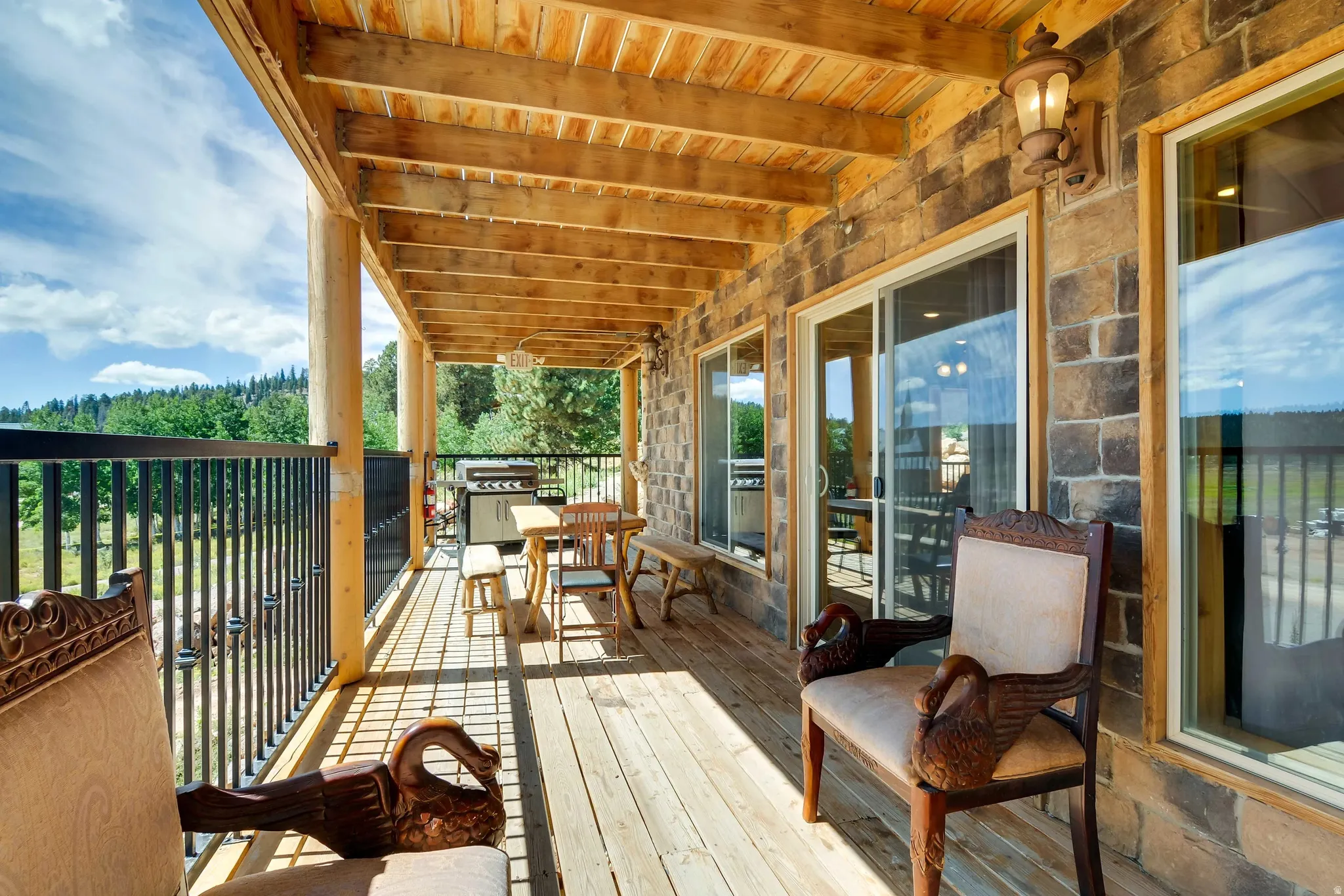 Expansive covered wood-finish deck with exposed beam ceiling, log posts, and black metal railing