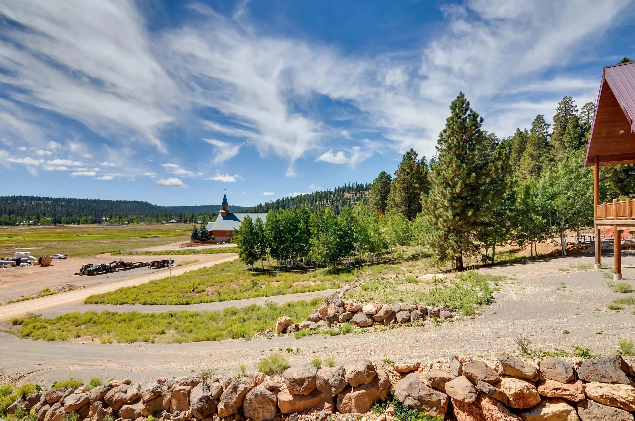 Terraced grounds featuring a rock retaining wall, mature pine trees, and a gravel driveway