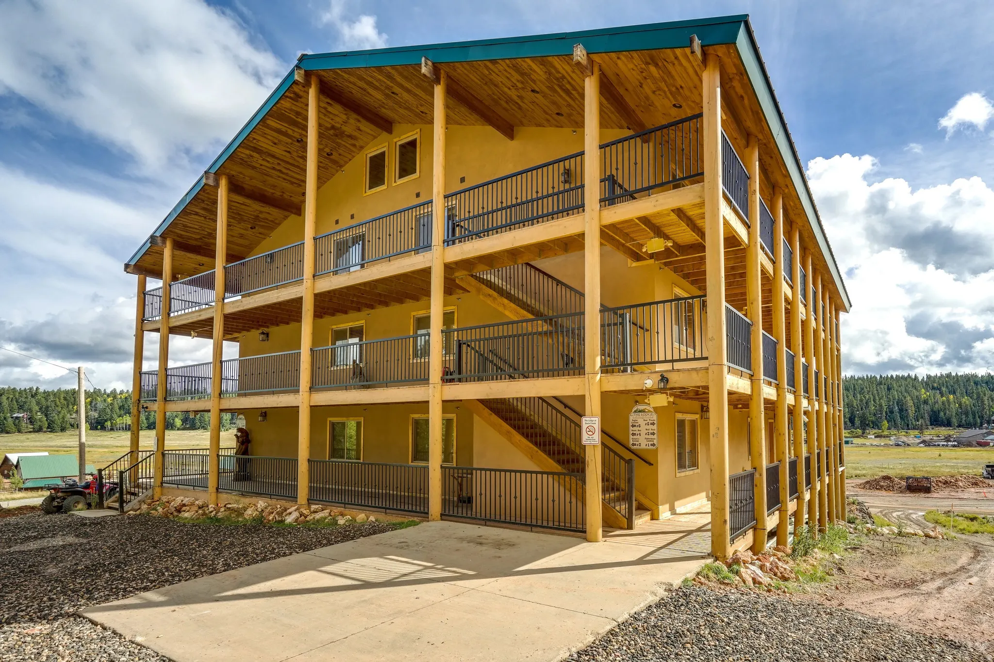 Three-story exterior featuring a turquoise roof, wood-finish columns, stucco siding, multiple balconies with black railings, and a concrete driveway