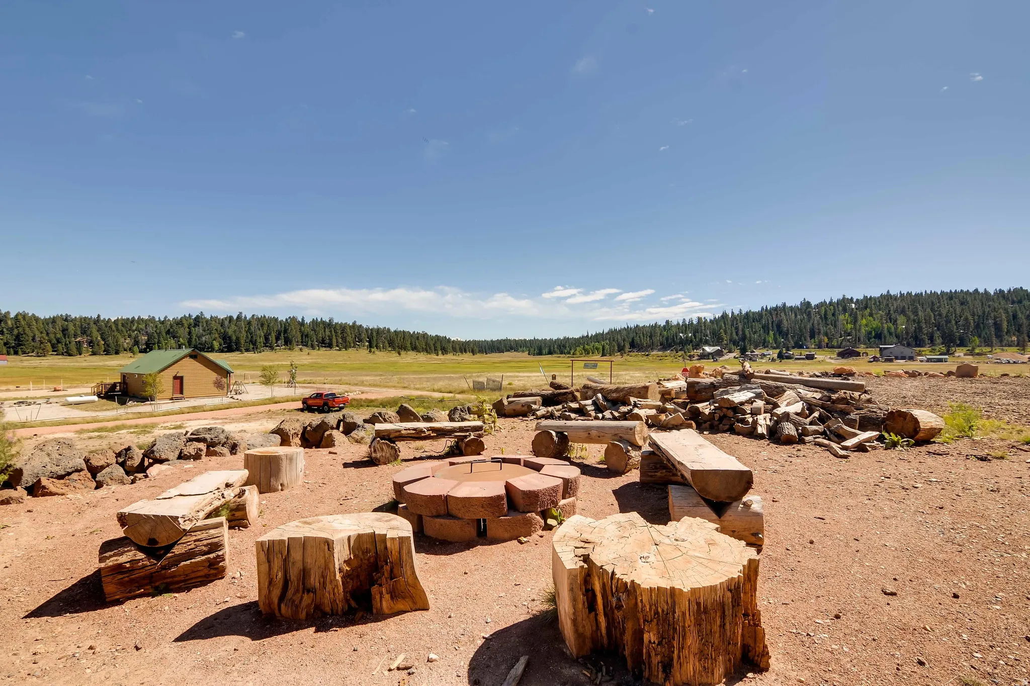 Outdoor gathering space featuring wood stump seating, a stone fire pit, and expansive natural landscape