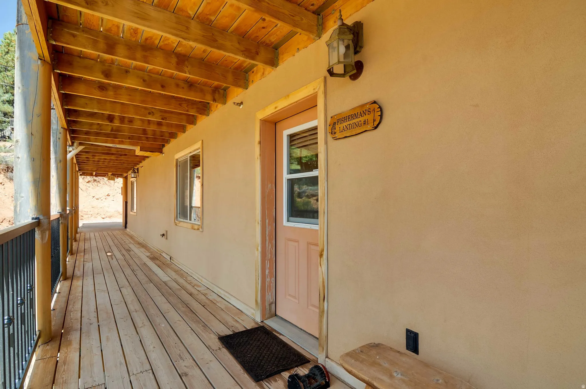 Expansive wood-finish porch with exposed wood ceiling beams, stucco exterior, and black metal railing