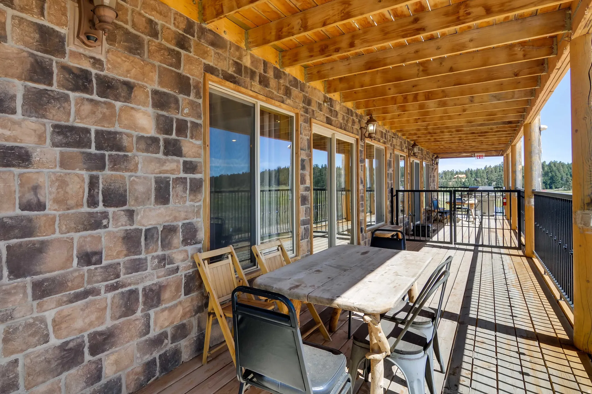 Spacious covered deck featuring a natural wood ceiling, wood-finish flooring, and a stone-clad exterior wall