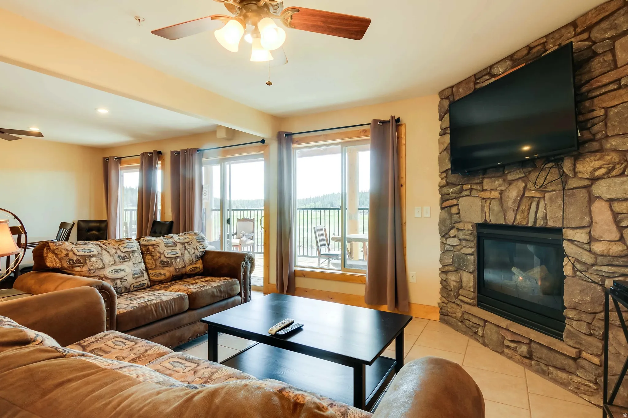 Spacious living area featuring a floor-to-ceiling stone fireplace, light tile flooring, and multiple sliding glass doors leading to an exterior balcony