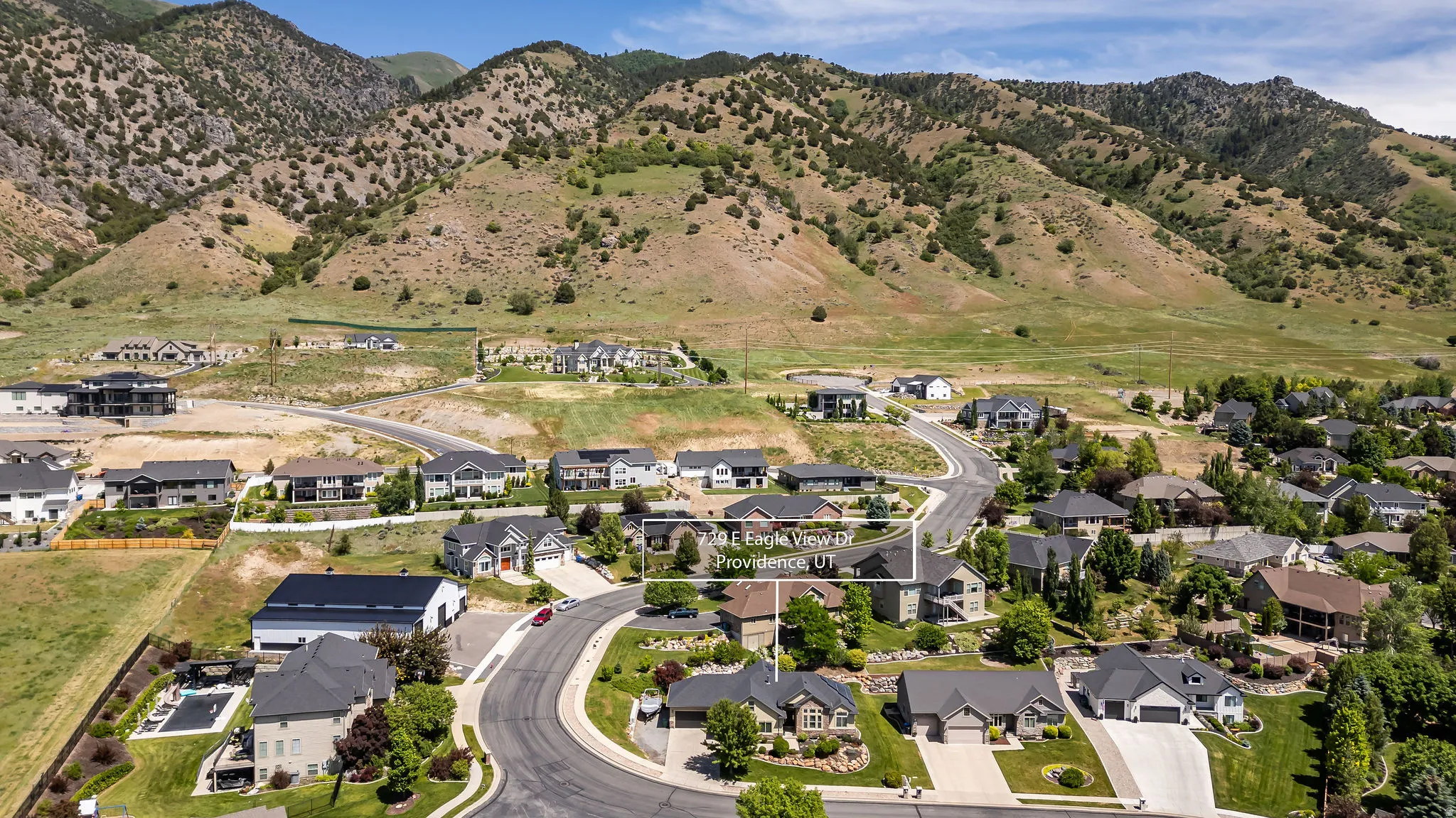 Residential neighborhood featuring a paved street, mature trees, and landscaping, with a mountainous backdrop