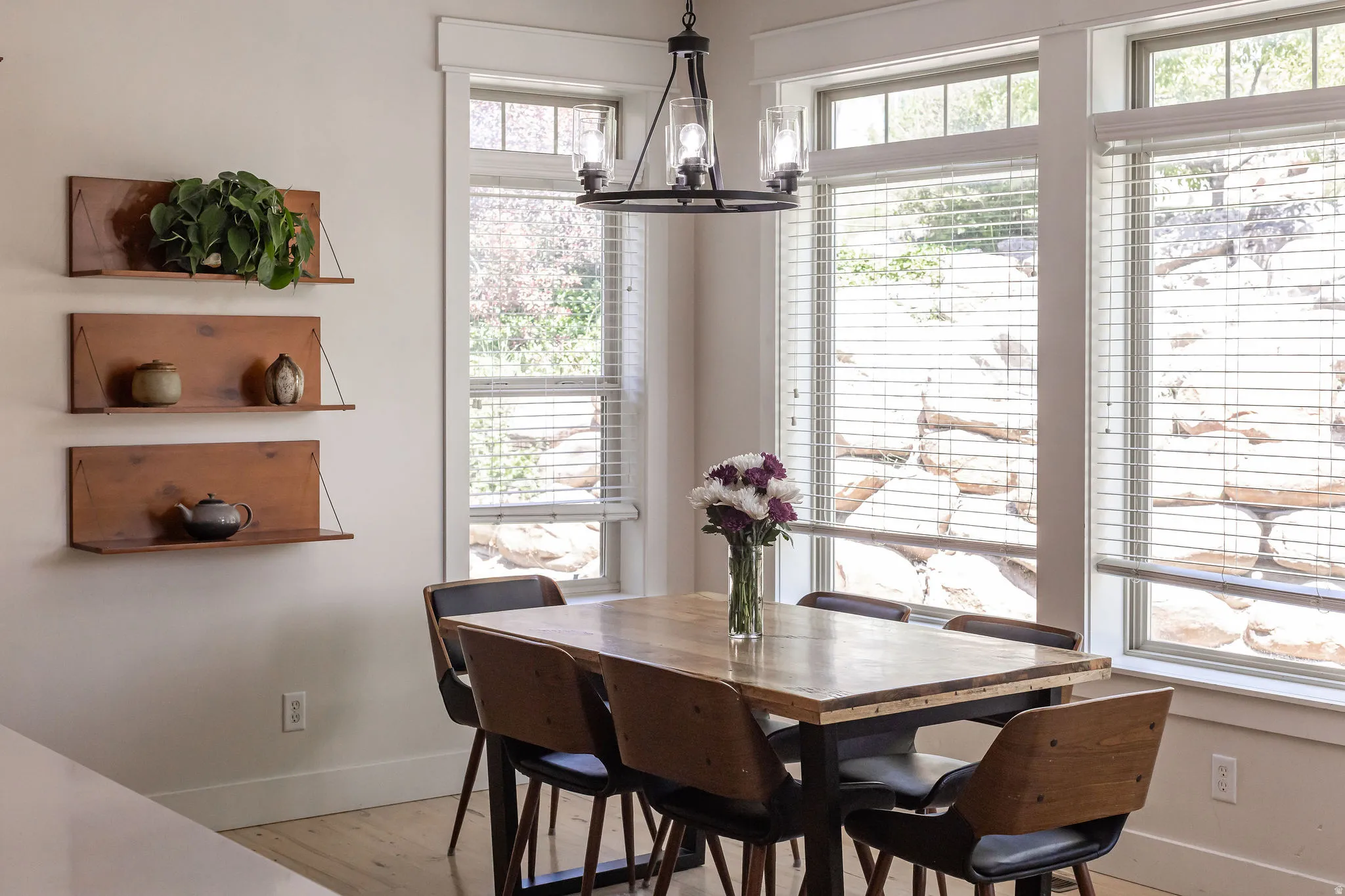 Dining area featuring multiple windows with blinds, a prominent chandelier with clear glass shades, wood-finish flooring, and built-in wall shelving