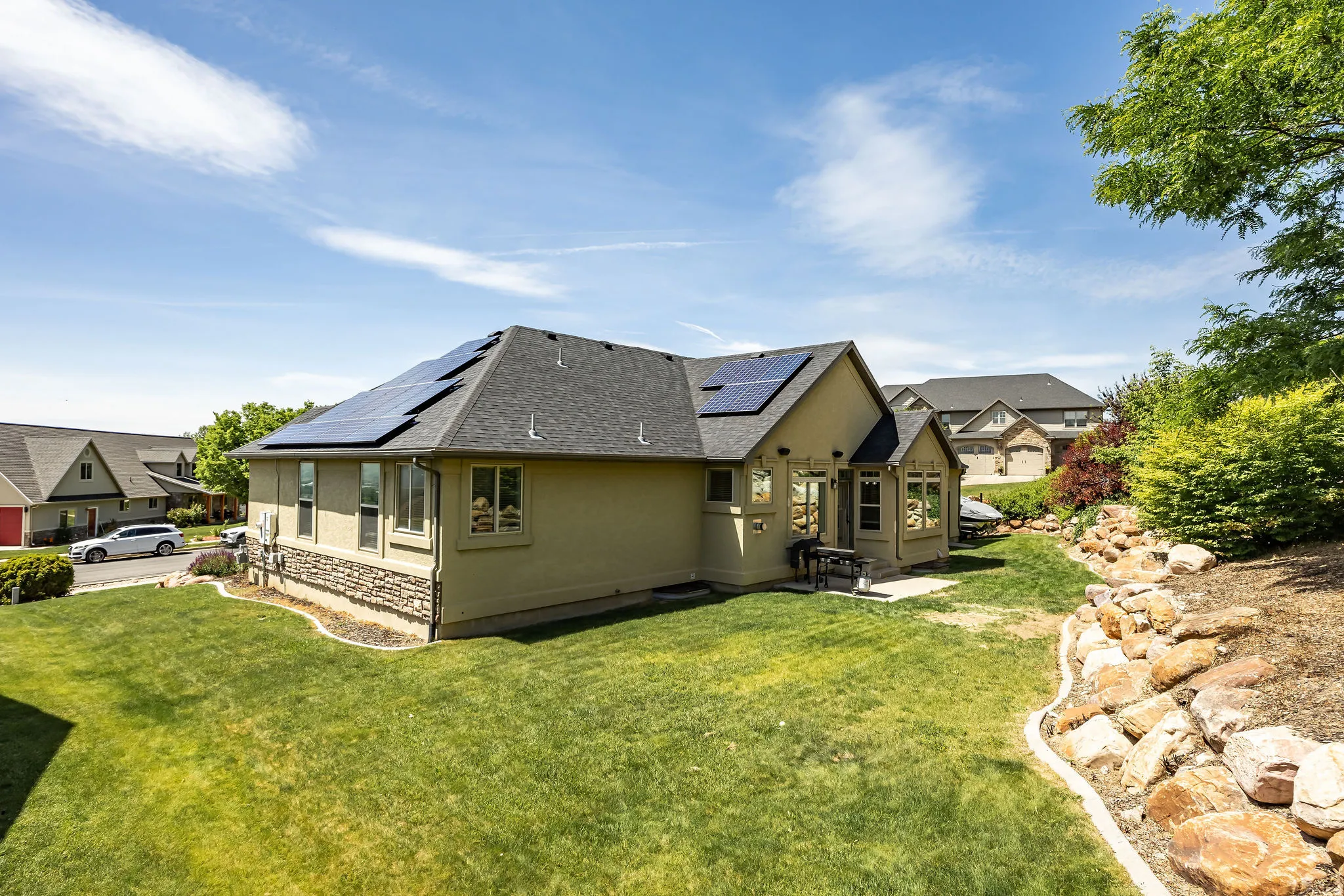 Rear exterior featuring a well-maintained lawn, solar panels, stone accent siding, and established landscaping