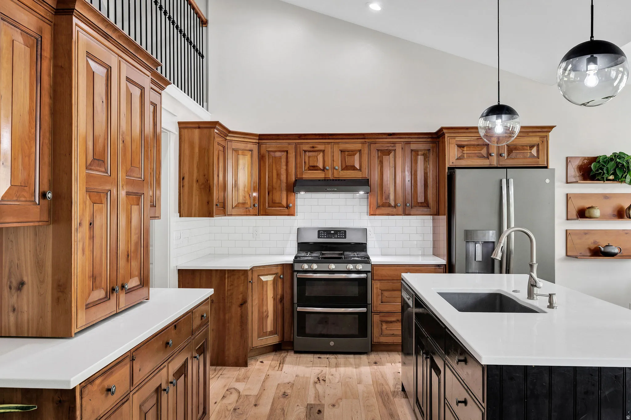 Open-concept kitchen featuring extensive wood cabinetry, white countertops, subway tile backsplash, stainless steel appliances, and an island with a built-in sink