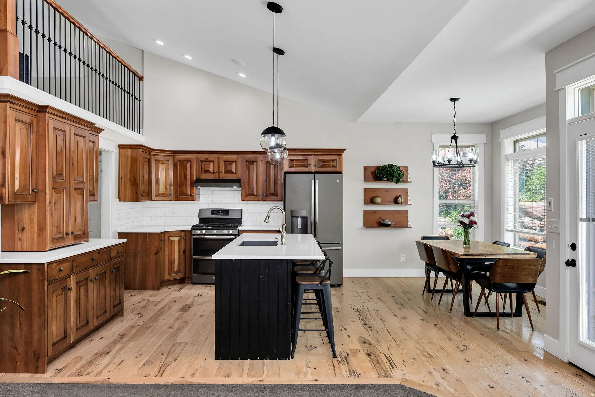Open-concept kitchen and dining area featuring wood-finish flooring, vaulted ceilings, and a second-story interior balcony with black iron railings