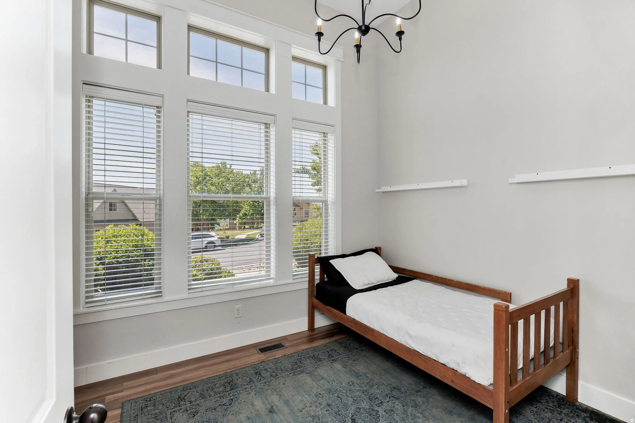 Room featuring multiple windows with blinds, wood-finish flooring, and a black chandelier