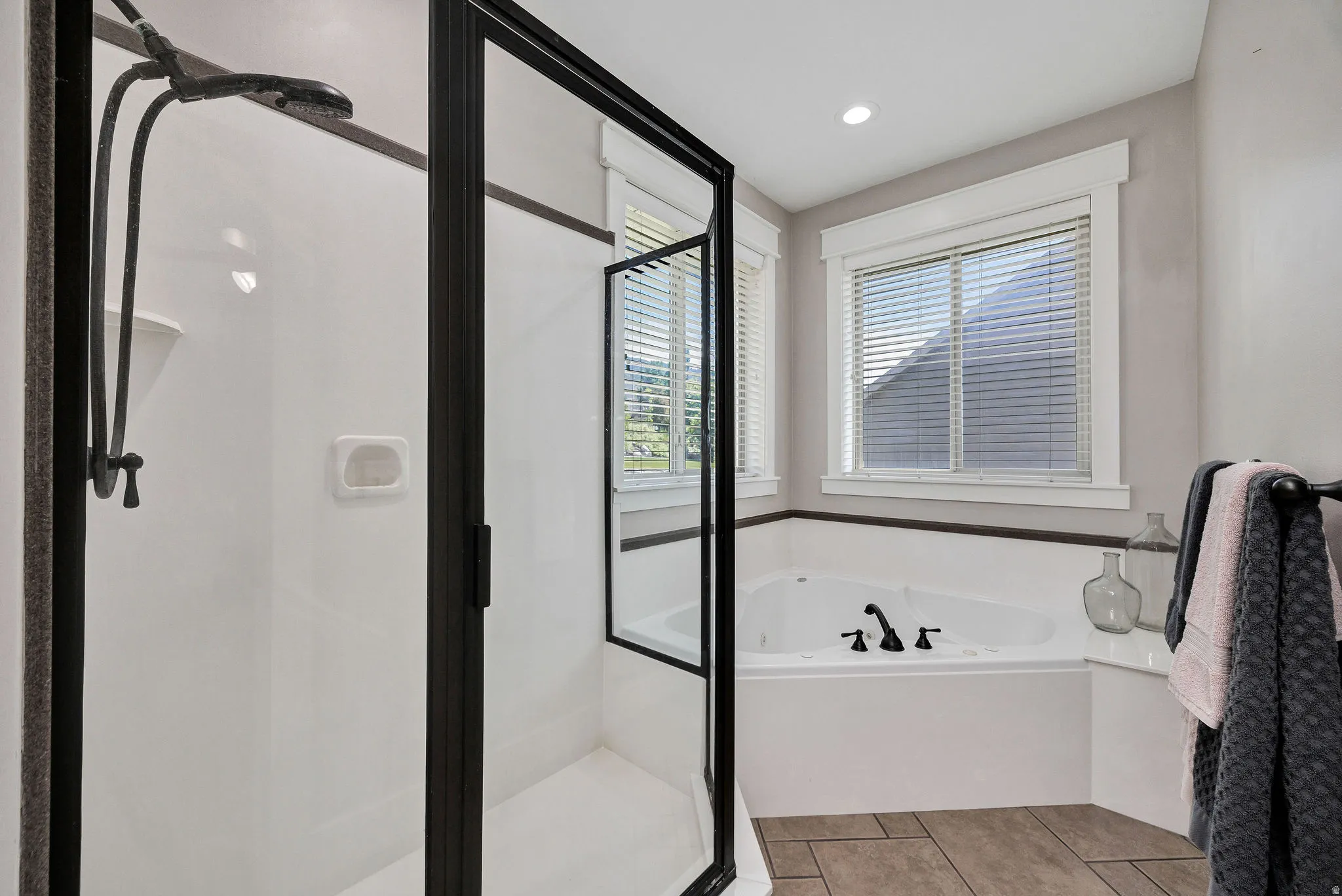 Spacious bathroom featuring a corner soaking tub with matte black fixtures, a walk-in shower with a black-framed glass enclosure, and wood-finish flooring