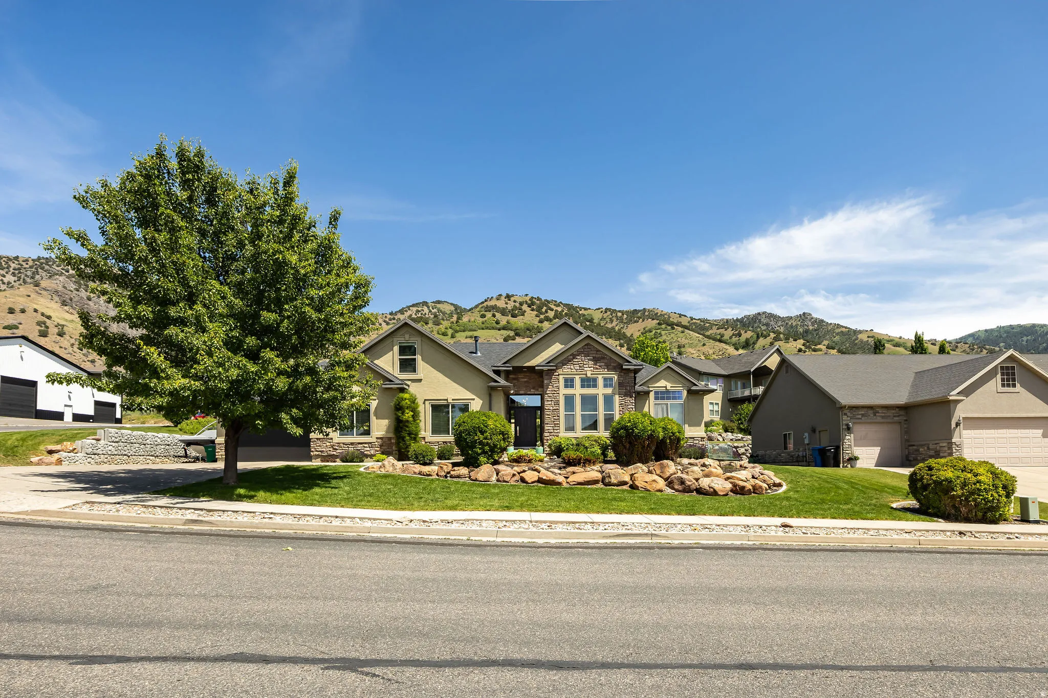 Ranch-style residence featuring a combination of stucco and stone exterior, an attached two-car garage, and a landscaped front yard with mature trees and shrubbery