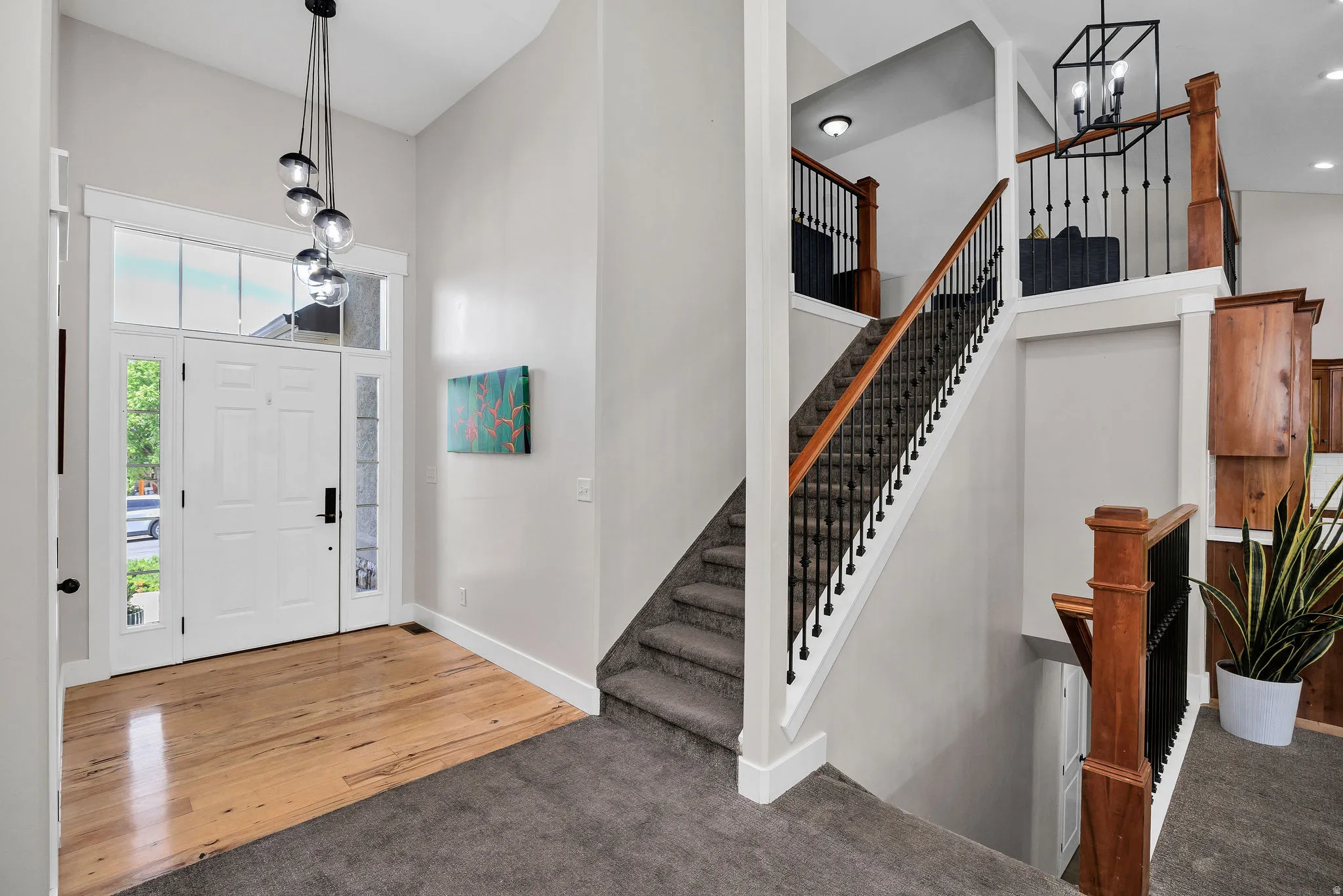 Two-story foyer featuring a white paneled entry door with sidelights and transom windows, wood-finish flooring, and a multi-pendant light fixture
