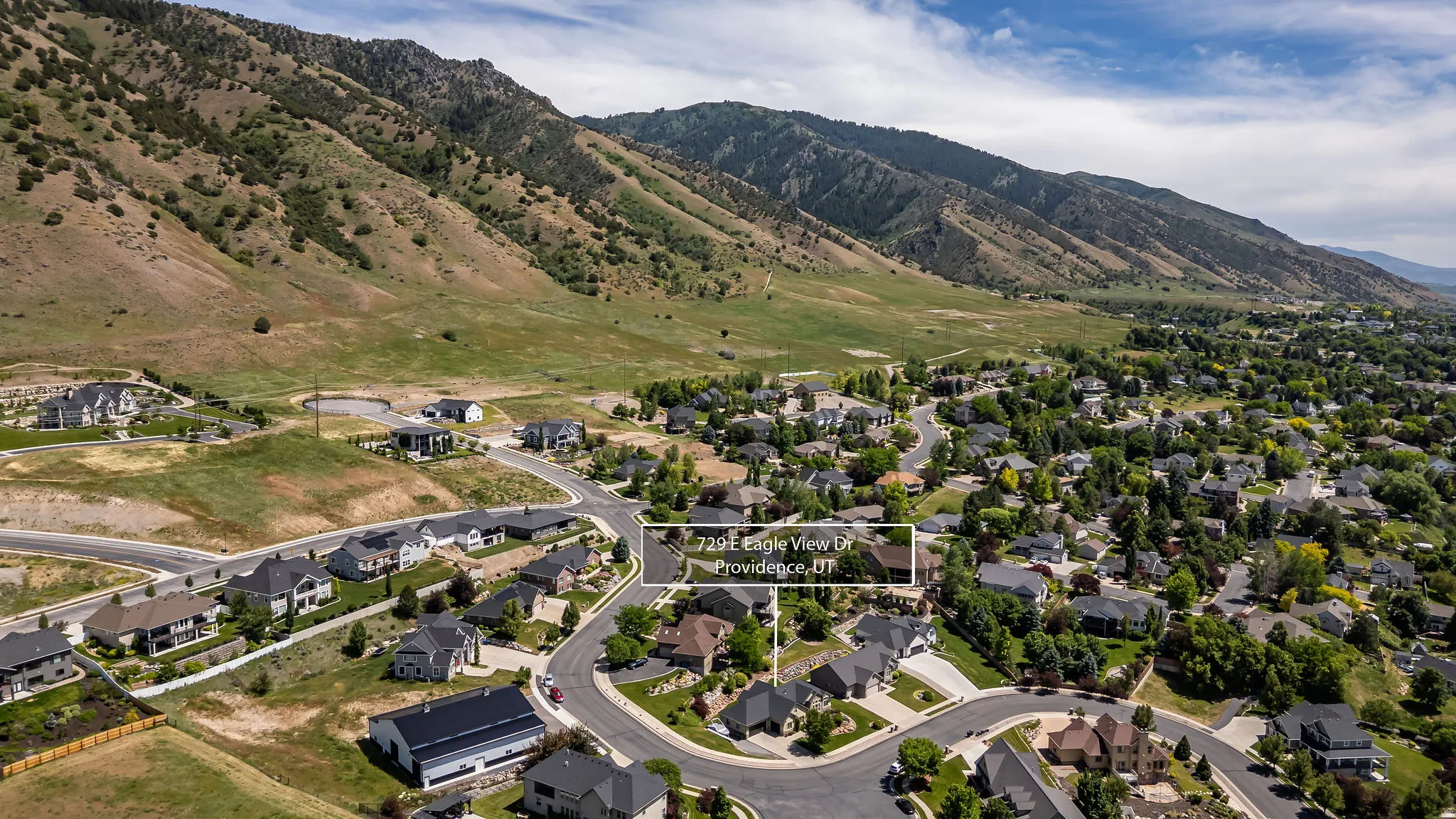 Aerial perspective showcasing residential properties nestled at the base of a verdant mountain range, with a prominent property highlighted on a curved street