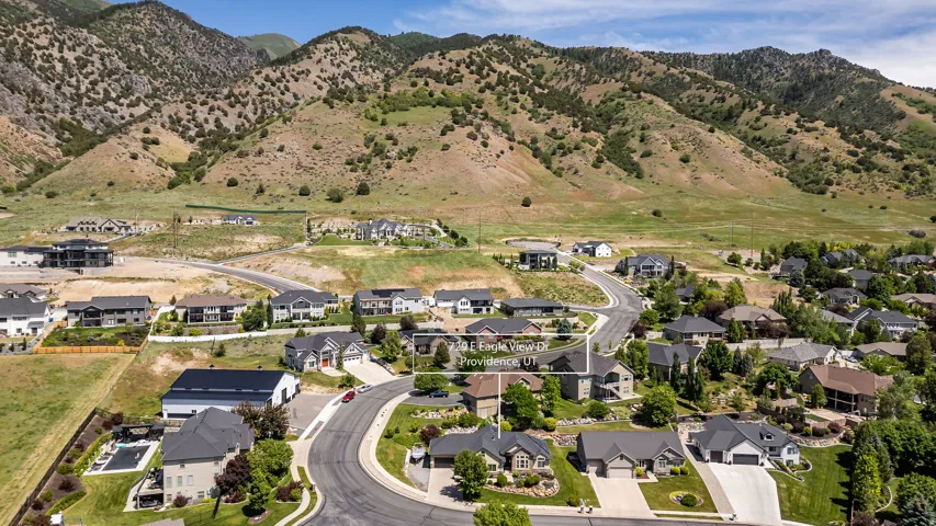 Residential neighborhood featuring a paved street, mature trees, and landscaping, with a mountainous backdrop