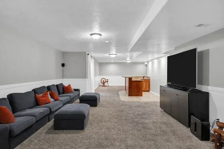 Finished basement featuring plush carpet flooring, recessed lighting, and a built-in wet bar with wood cabinetry and stone countertops