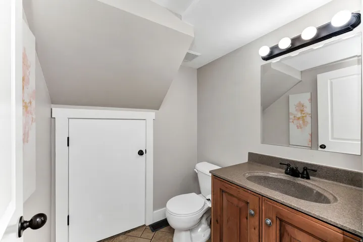 Powder room featuring a wood-finish vanity with an integrated sink, a dark countertop, and dark-finish hardware