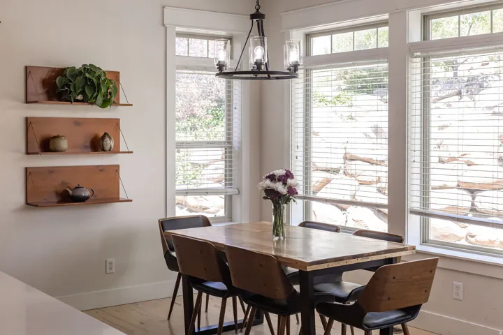 Dining area featuring multiple windows with blinds, a prominent chandelier with clear glass shades, wood-finish flooring, and built-in wall shelving