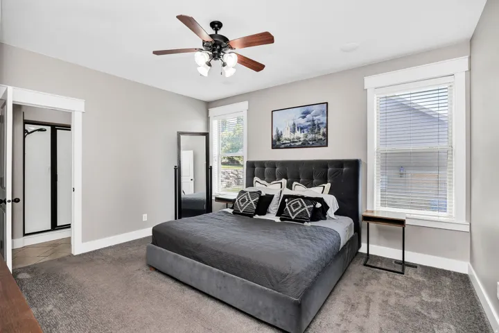 Carpeted bedroom featuring a ceiling fan with integrated lighting, two windows with blinds, and white trim throughout