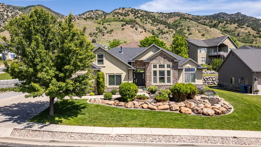Exterior property featuring stone veneer accents, an asphalt shingle roof, a two-car garage, established landscaping, and a mountainous background