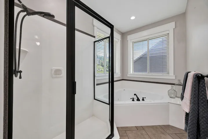 Spacious bathroom featuring a corner soaking tub with matte black fixtures, a walk-in shower with a black-framed glass enclosure, and wood-finish flooring