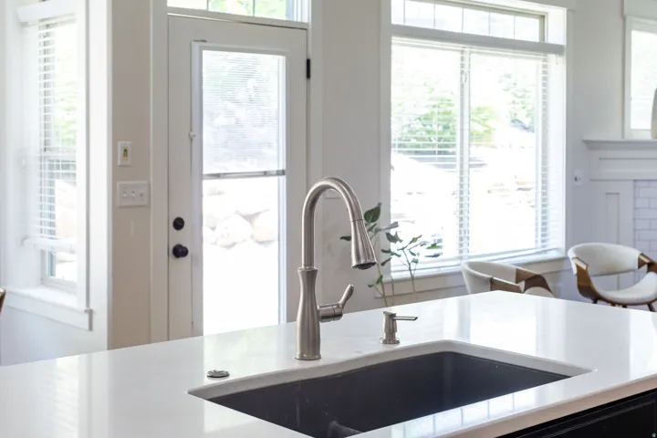 Kitchen island featuring a dark composite sink, gooseneck faucet, and integrated soap dispenser
