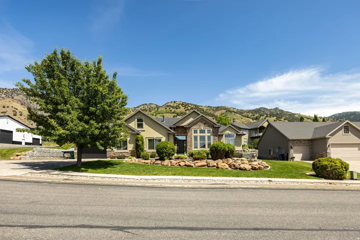 Ranch-style residence featuring a combination of stucco and stone exterior, an attached two-car garage, and a landscaped front yard with mature trees and shrubbery