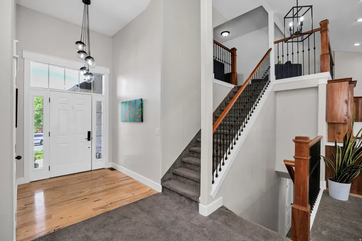 Two-story foyer featuring a white paneled entry door with sidelights and transom windows, wood-finish flooring, and a multi-pendant light fixture