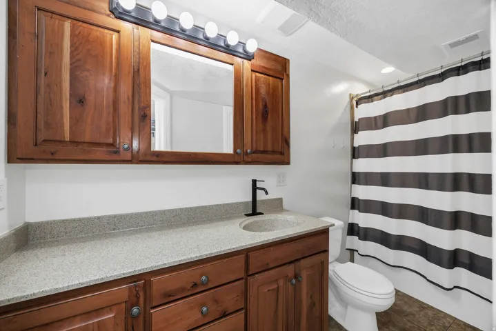 Bathroom featuring a wood-finish vanity with a light speckled countertop, undermount sink, and black wall-mounted faucet