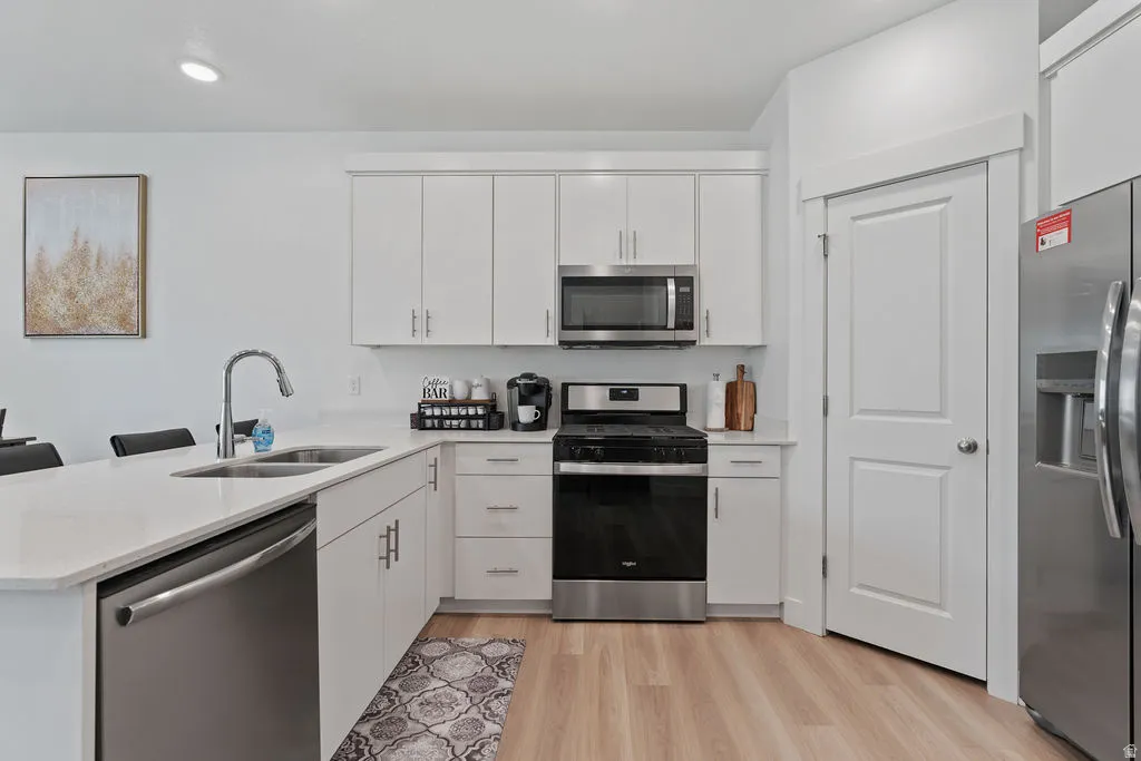 Modern kitchen featuring white cabinetry, stainless steel appliances, a large island with sink, quartz countertops, and wood-finish flooring