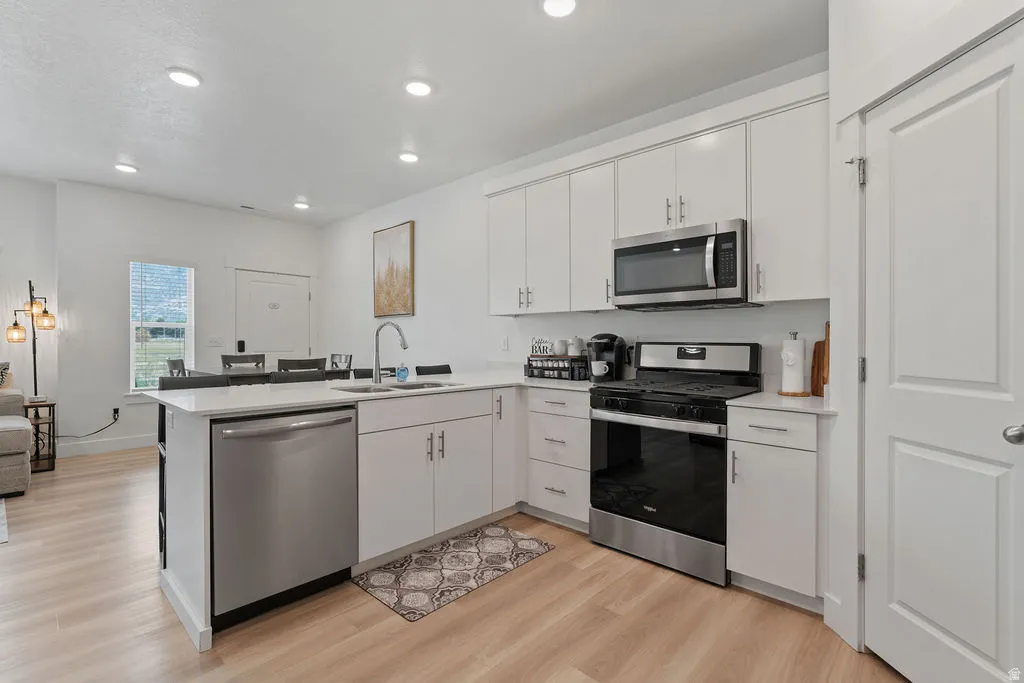 Modern kitchen featuring white cabinetry, stainless steel appliances, light wood-finish flooring, recessed lighting, and a kitchen island with integrated sink