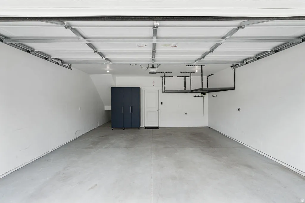 Spacious garage featuring a concrete floor, built-in overhead storage racks, recessed lighting, and a dark blue storage cabinet